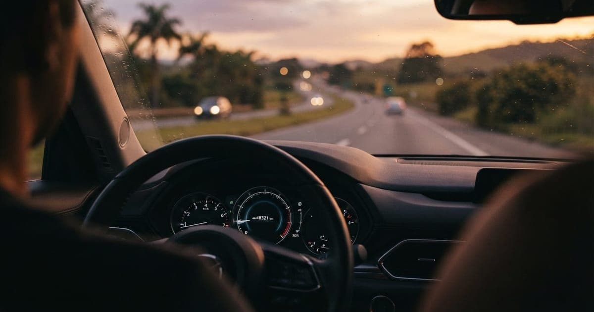 Painel de carro moderno indicando odômetro em destaque com fundo desfocado de rodovia brasileira ao entardecer