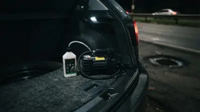 Kit de reparo de pneu com compressor de ar de 12V e frasco de selante químico posicionado sobre carpete de porta-malas