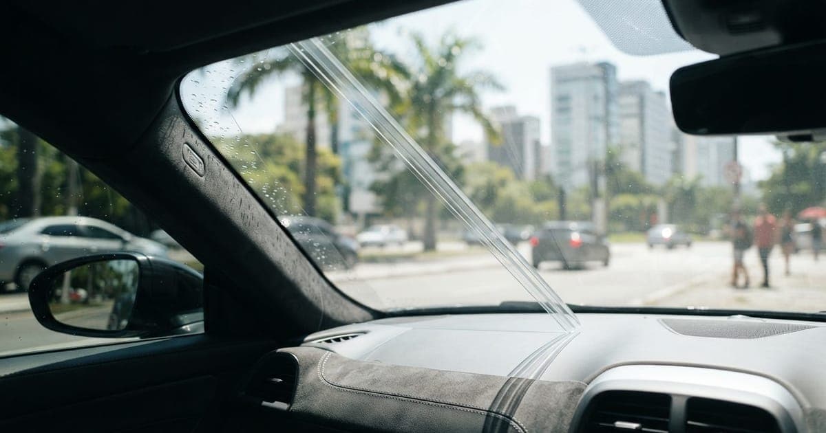 Detalhe de para-brisa de carro com película transparente aplicada, mostrando isolamento térmico e alta visibilidade