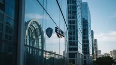 Fachada de prédios corporativos modernos com logos da Warner Bros e Amazon refletidos em vidro azulado sob luz do dia.